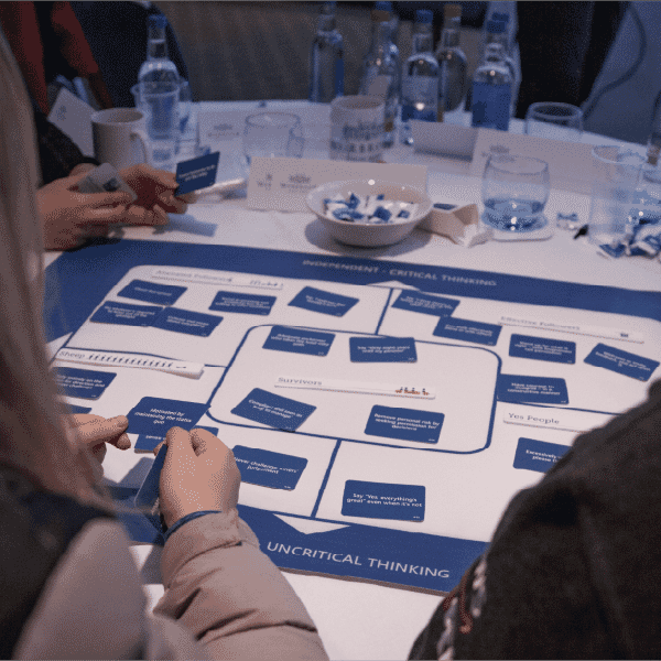 Participants working together around a table during a workshop, using learning materials as part of a graduate programme focused on critical thinking and collaboration.