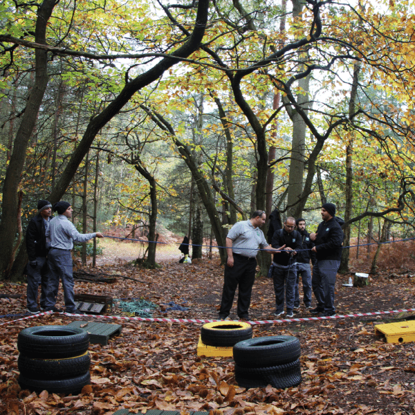 Group of professionals taking part in an outdoor team challenge in a woodland setting, demonstrating collaboration and transforming leadership through experiential learning.