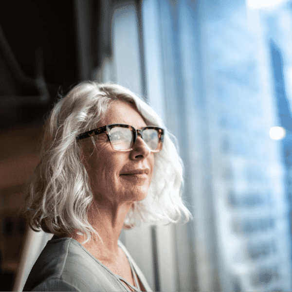 Experienced woman leader standing by a window and looking ahead with confidence, reflecting empowering women leaders.