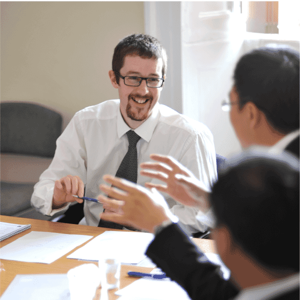 “A consultant smiling and engaging in discussion with clients around a table during a facilitated workplace session.”