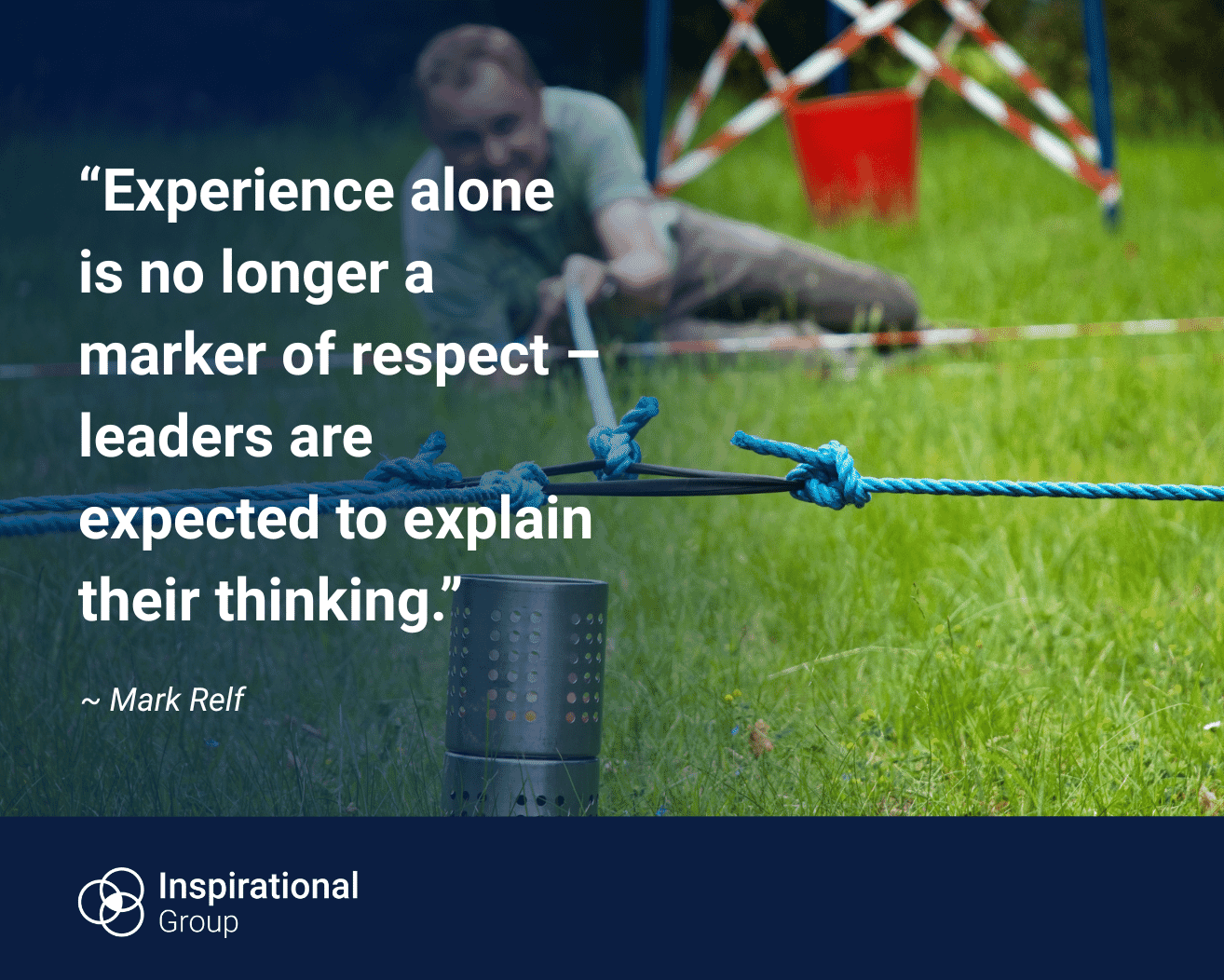 A person lying on grass reaching forward to adjust a rope, with a small camping stove in the foreground as part of an outdoor group activity. Overlaid text reads: “Experience alone is no longer a marker of respect – leaders are expected to explain their thinking.” The quote is attributed to Mark Relf, with Inspirational Group branding at the bottom.
