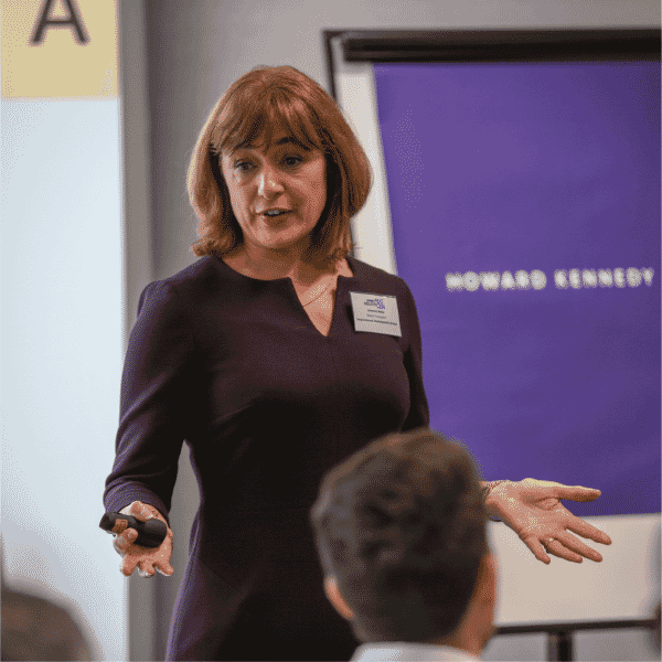Johanne Malin facilitating and speaking to a group during a leadership development session, gesturing while presenting beside a flip chart.”