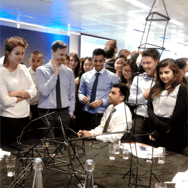 “Participants gathered around a table taking part in a collaborative leadership exercise using a physical structure-building activity.”