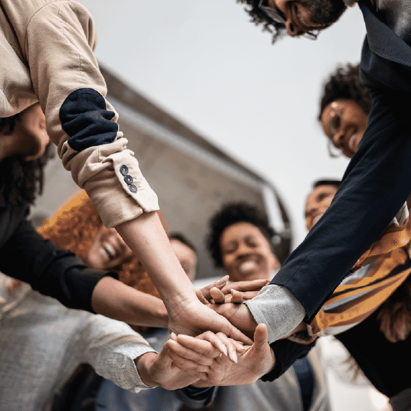 “Diverse group of people standing in a circle with hands stacked together in a gesture of teamwork.”
