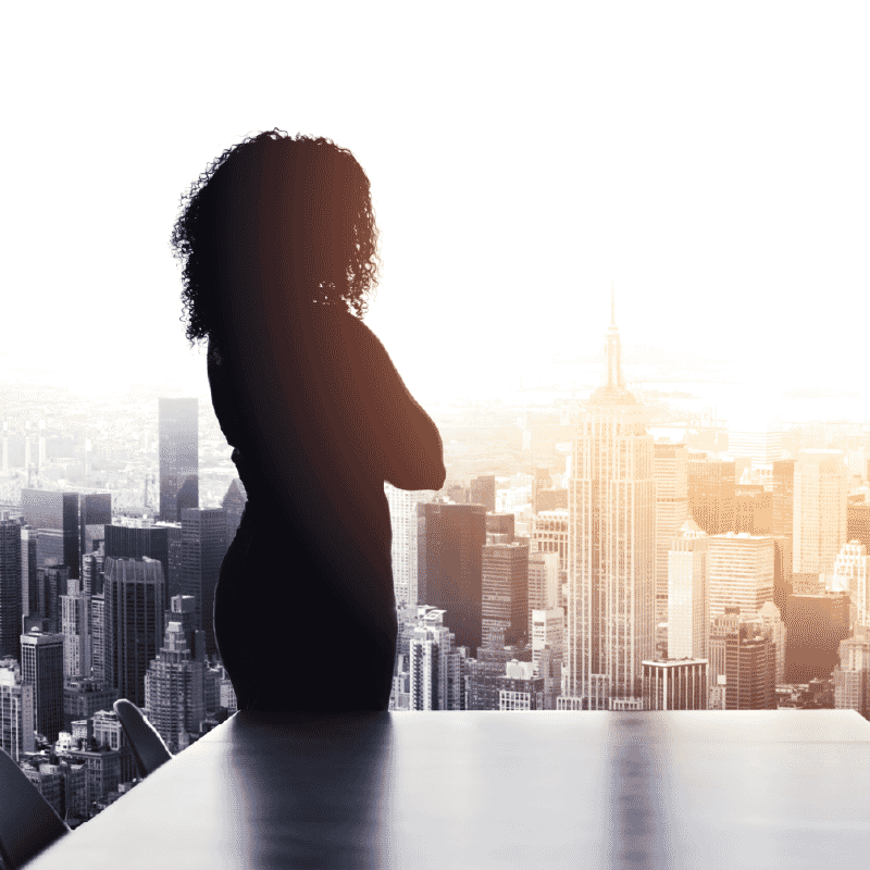 “Silhouette of a professional standing by a window, looking out over a city skyline in contemplation.”