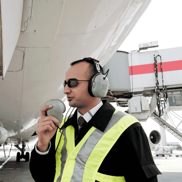 Airport operations professional in high-visibility vest communicating on the stand, representing frontline leadership in the aviation sector.